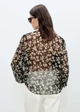 Blusa de gasa negra con estampado de margaritas blancas, cuello pico con lazo y cierre de botones frontal.
