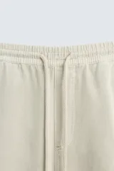 Pantalón color arena de corte recto, confeccionado en tejido de algodón y lino. Cuenta con cintura elástica ajustable con cordón, bolsillos delanteros y traseros de parche.