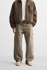 Pantalón color marrón con efecto lavado, corte relaxed fit, cinco bolsillos, aplicación de tira y bolsillo multifunción en perneras, cierre frontal con cremallera y botón.