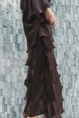 Vestido midi color marrón oscuro confeccionado en hilatura con viscosa y algodón. Tiene cuello redondo, manga corta y bajo con volantes desflecados y aberturas laterales.