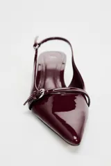 Zapato destalonado color borgoña charol, con tacón kitten y punta fina. Presenta una tira trasera con hebilla ajustable y detalle de hebilla metálica en la parte delantera.