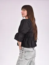 Blusa negra con escote mao y mangas 3/4 con volantes. Presenta detalle de frunces en el frente y lazos para ajustar.