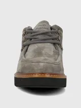 Zapato estilo mocasín o derby de mujer, color gris, confeccionado en gamuza. Presenta suela plataforma negra con borde de cuero marrón cosido y cordones grises que pasan por ojales metálicos dorados.