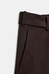 Pantalón ancho de tiro medio color marrón oscuro, confeccionado en tejido con lana. Presenta pinzas delanteras, cinturón ajustable con hebilla metálica y bolsillos cargo de plastrón en las piernas.