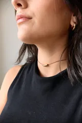 Gargantilla con tiento de hilo encerado color borgoña y dije de acero quirúrgico hipoalergénico plateado en forma de tubo.