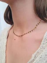 Collar dorado con cadena fina y pequeños colgantes negros.