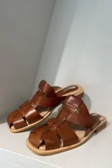 Zueco marrón de cuero vacuno con diseño de tiras entrecruzadas y suela plana.