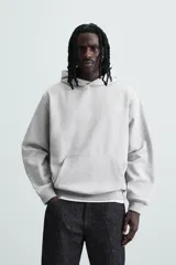 Sudadera con capucha color crudo, de corte relajado, confeccionada en tejido de algodón con interior rizado. Cuenta con cuello con capucha, manga larga, bolsillo frontal tipo canguro y acabados en rib.