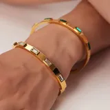 Brazalete rígido dorado con incrustaciones de circonitas rectangulares.