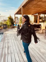 Campera marrón de cuero con cuello camisero, cierre frontal con botones a presión, bolsillos laterales y mangas largas con flecos.