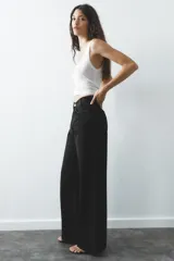 Pantalón de jean celeste de tiro alto, corte wide leg y largo hasta el tobillo. Presenta un diseño asimétrico en la cintura con cierre frontal cruzado con cremallera y botones metálicos.