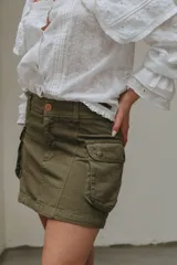 Minifalda de jean azul con corte en A y bolsillos tipo cargo con solapa y botón. Tiene un chaleco haciendo juego con cierre de botones.