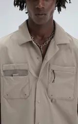 Camisa beige de manga corta, estilo técnica, confeccionada en microfibra liviana. Con doble bolsillo frontal y broches en lugar de botones.