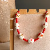 Collar corto con cuentas de cerámica blanca con diseños florales en rojo, naranja y violeta, separadas por pequeñas cuentas rojas.