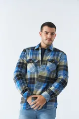Sobrecamisa de algodón para hombre con interior de corderito, estampado a cuadros en tonos negro, blanco y azul. Tiene cierre de botones, bolsillos tipo cartera y logo en goma. El modelo usa talle M.