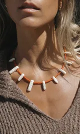 Collar corto con cuentas tubulares de coral naranja y colmillos de piedra fósil blanca.