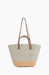 Bolso tipo tote de tela tejida color crudo con estampado de manchas negras y base de rafia. Tiene doble asa de cuero marrón.