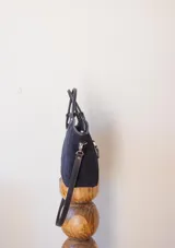 Cartera negra de gamuza con forro interior y correa larga desmontable.