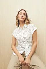 Camisa blanca con broderie, de manga corta, cuello clásico, botones al frente y lazo regulable en la cintura.