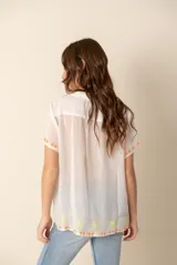 Camisa blanca de seda con bordados florales multicolor, cuello camisero y mangas cortas.