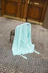 Bata verde agua con rayas verticales azules, confeccionada en lino. Tiene corte holgado, mangas largas y cinturón para ajustar en la cintura.