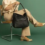 Cartera negra de cuero sintético con apertura superior y cierre con solapa. Tiene un bolsillo frontal con broche magnético y cierre, dos bolsillos internos y un bolsillo divisor en el forro. Incluye bolsillos laterales con cierre y correa larga regulable.