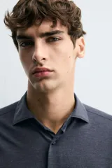 Camisa de manga larga con cuello italiano y cierre frontal de botonadura. Presenta un patrón de rayas verticales finas en tonos blanco y verde claro.