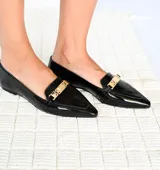 Mocasines negros de charol con punta fina y aplique metálico dorado en el empeine.