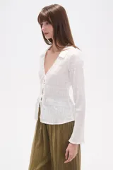 Blusa blanca de algodón con textura fruncida, manga larga y escote en V con lazo ajustable en el centro del busto.