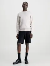 Sweater color beige de Calvin Klein, confeccionado en mezcla de tencel con elasticidad añadida. Tiene cuello redondo, puños y bajo de canalé, y etiqueta con logo de Calvin Klein por encima del bajo.