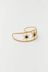 Pulsera dorada tipo brazalete con diseño de soles con centro de piedra negra.