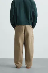 Pantalón color caqui de corte amplio, con pinzas en la cintura, bolsillos laterales y traseros con botón.