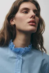 Camisa blanca de algodón con cuello con volantes y mangas largas con puños fruncidos.