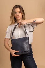 Bandolera de hombro color gris claro, con solapa frontal y correa ajustable. Presenta un diseño simple y práctico, ideal para uso diario.