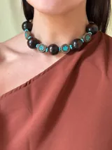 Collar corto con cuentas grandes de madera color marrón oscuro, separadores de metal con incrustaciones de turquesas y cuentas pequeñas turquesas. Cierre con cadena de acero quirúrgico y ganchito para regular el largo.