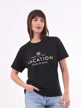 Remera negra de algodón con cuello redondo y mangas cortas. Estampado frontal con la frase "World Tour Vacation State of Mind" en letras de colores y un pequeño dibujo de una palmera.