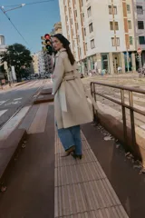 Gabardina larga color beige, con cuello solapa, manga larga con trabillas en hombros y cierre frontal cruzado con botones negros. Incluye cinturón a tono anudado.