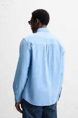 Camisa celeste de lyocell y algodón, corte relaxed fit, cuello solapa, manga larga con puños abotonados, bolsillo de parche en el pecho y cierre frontal con botones.