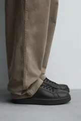 Zapatilla urbana de cuero sintético color negro, con cordones y suela de plataforma.