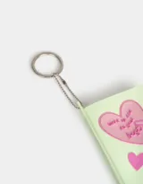 Llavero con dije de libreta de silicona color verde claro, con diseño en relieve de un corazón con la frase "Wake up and do your best", un batido y un corazón pequeño. Incluye cadena metálica con aro.