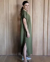 Vestido largo color crudo con cuello redondo y mangas cortas con ribete negro. Tiene corte recto y aberturas laterales en el ruedo.