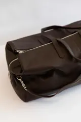 Bolso de viaje tipo weekender color marrón cuero, confeccionado en cuero vacuno. Tiene doble asa de mano y correa bandolera regulable y extraíble. Cuenta con cierre superior de cremallera y herrajes plateados.