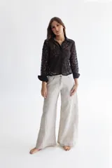 Pantalón de lino color greige, de piernas anchas, con cadera al cuerpo y cintura media. Presenta apliques de lino rayado en los costados.