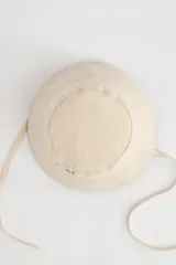 Gorro tipo bucket color beige con bordado frontal de la frase "Be Sunny" en marrón. Incluye cordones laterales ajustables.