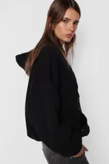 Buzo hoodie negro de frisa, corte oversize, con puños y cintura de rib al tono, capucha forrada y bolsillo canguro. Detalle de remaches en la boca del bolsillo, cierre metálico niquelado en el puño de las mangas, cordones con ojalillos y punteras personalizadas de marca. Cordones atracados en delantero con bordado de marca.