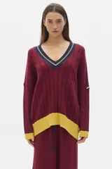 Sweater tejido de punto color crema, con cuello en V con borde negro y doble línea blanca, mangas largas con puños negros, diseño con trenzas en el frente y corte oversize.