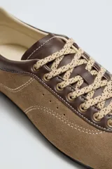 Zapato deportivo de piel color marrón claro con detalles en marrón oscuro y rojo. Presenta pespuntes en contraste, suela plana y cierre con cordones de colores. Colaboración especial Harry Lambert for Zara x Disney.