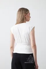 Top sin mangas color beige, confeccionado en tejido acanalado. Presenta hombreras definidas y un recorte fruncido bajo el busto que ajusta la silueta.