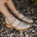 Zapato de cuero negro con detalle de charol, taco de madera con folia en cuero de 5cm, cierre YKK en talón, hebilla y elástico en el empeine.