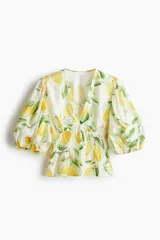 Blusa corta con escote en V pronunciado, elásticos finos en la cintura y peplum. Mangas globo cortas con elástico oculto en los puños. Estampado de limones y hojas verdes.